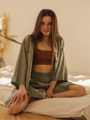 Free photo beautiful young caucasian woman sitting on mattress floor looking into camera indoors longhaired brunette wears top shirt and skirt home comfort concept