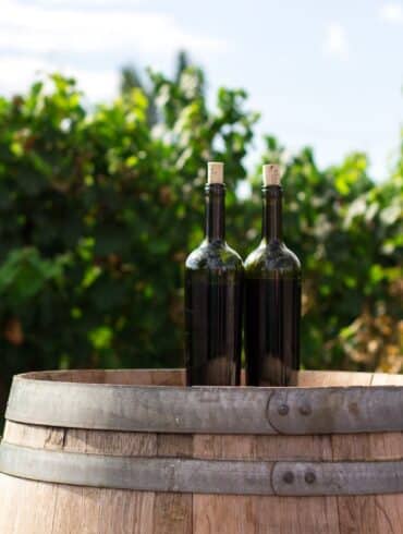 two black glass bottles on the top of the brown wooden barrel